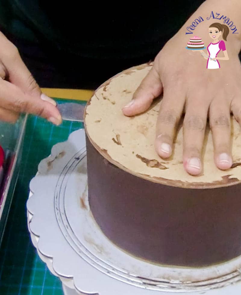 A person covering a cake with ganache.