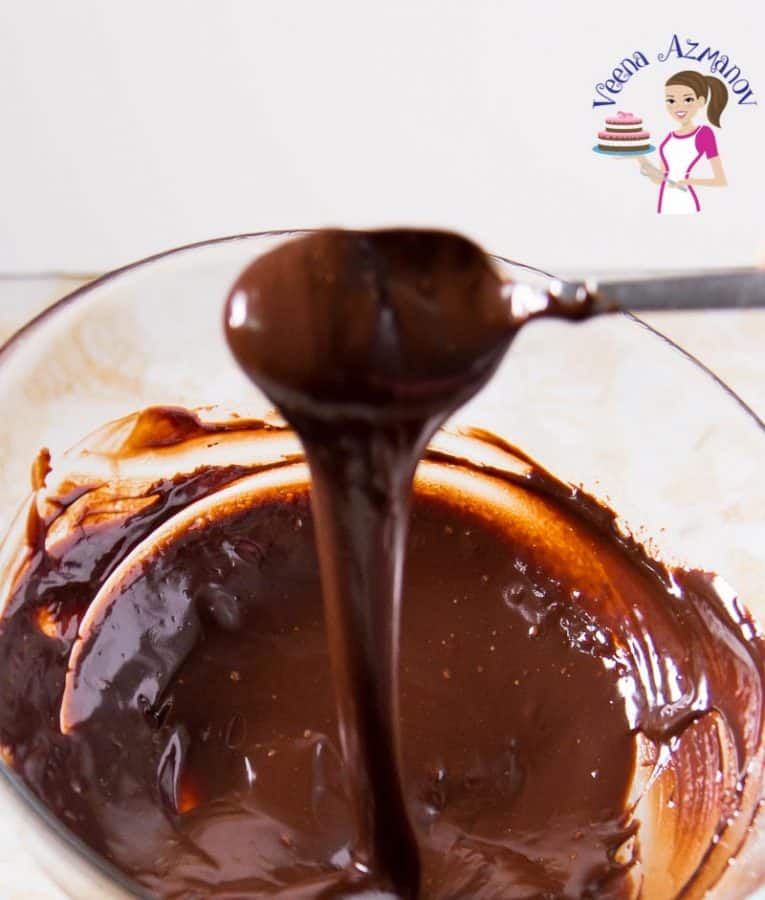 Chocolate ganache being mixed with a spoon in a glass bowl.