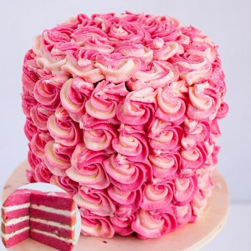 A frosted strawberry layer cake on a cake board.