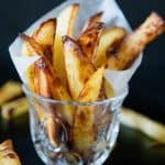 Potato wedges in a short glass with parchment.
