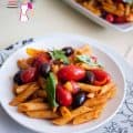 A plate of penne pasta with cherry tomatoes and olives.