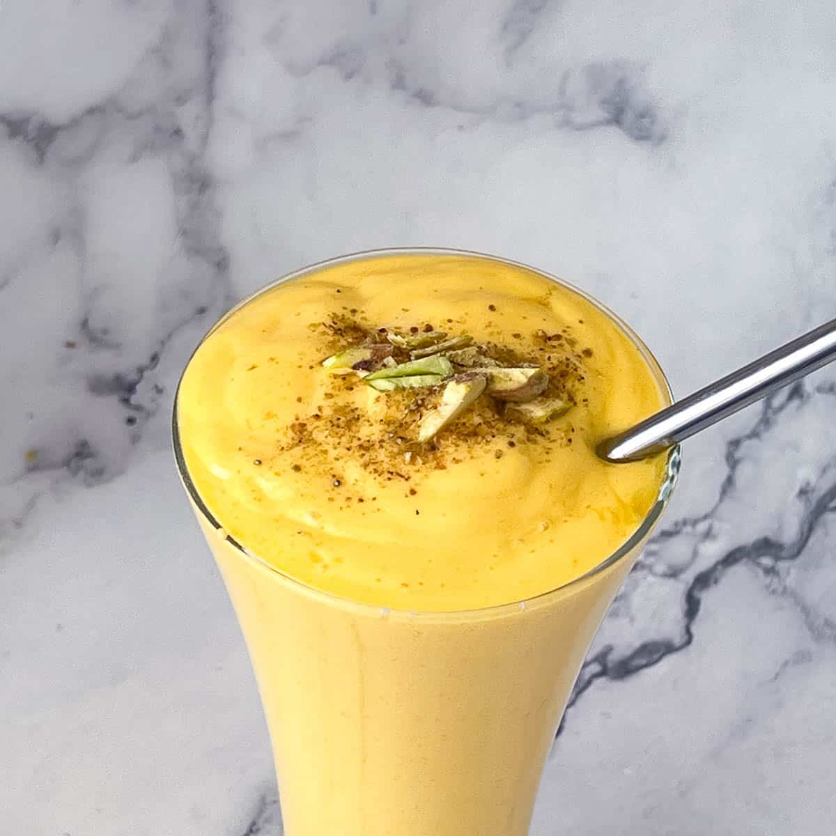Mango lassi garnished with pistachios and cardamom.