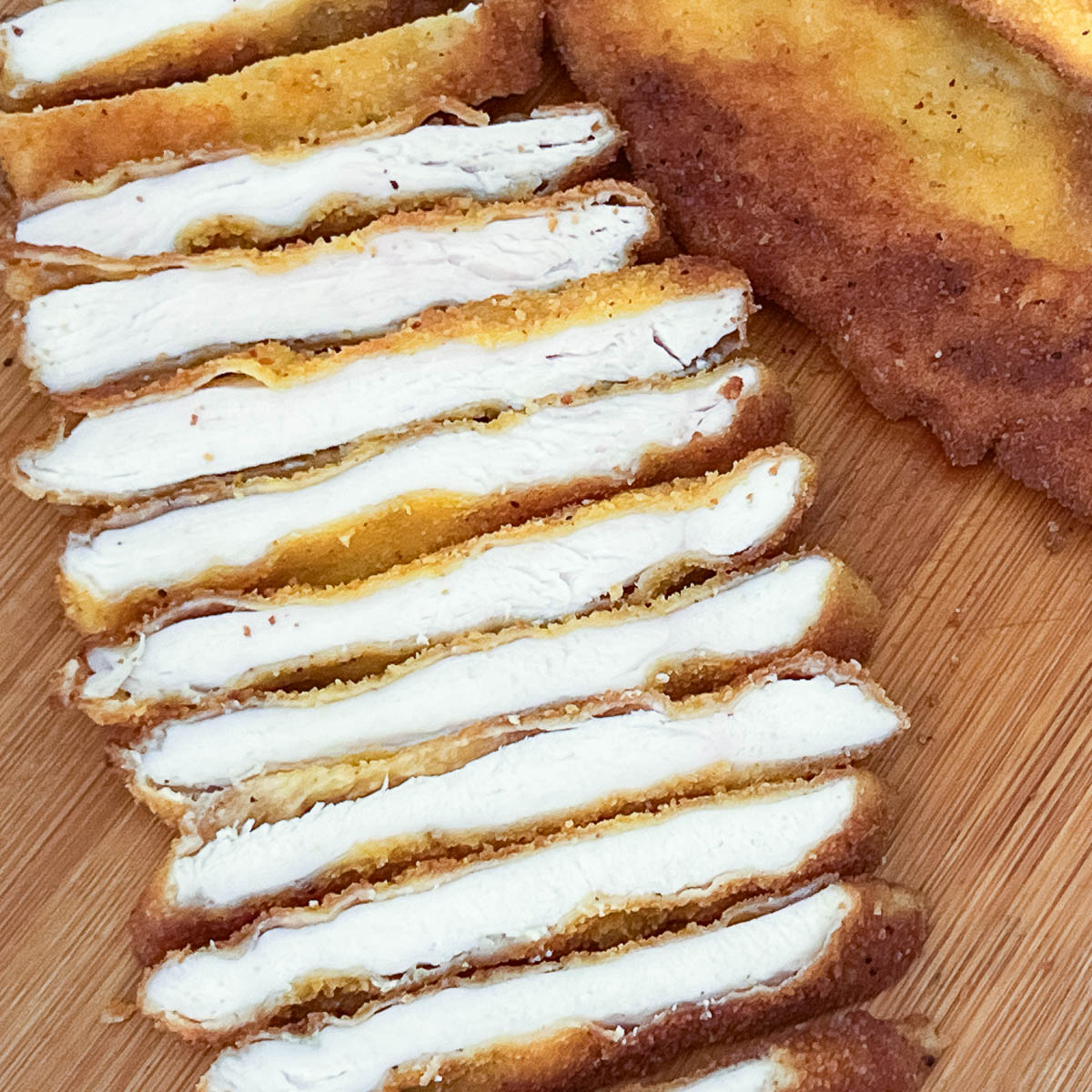 Sliced chicken schnitzel on a wooden board.