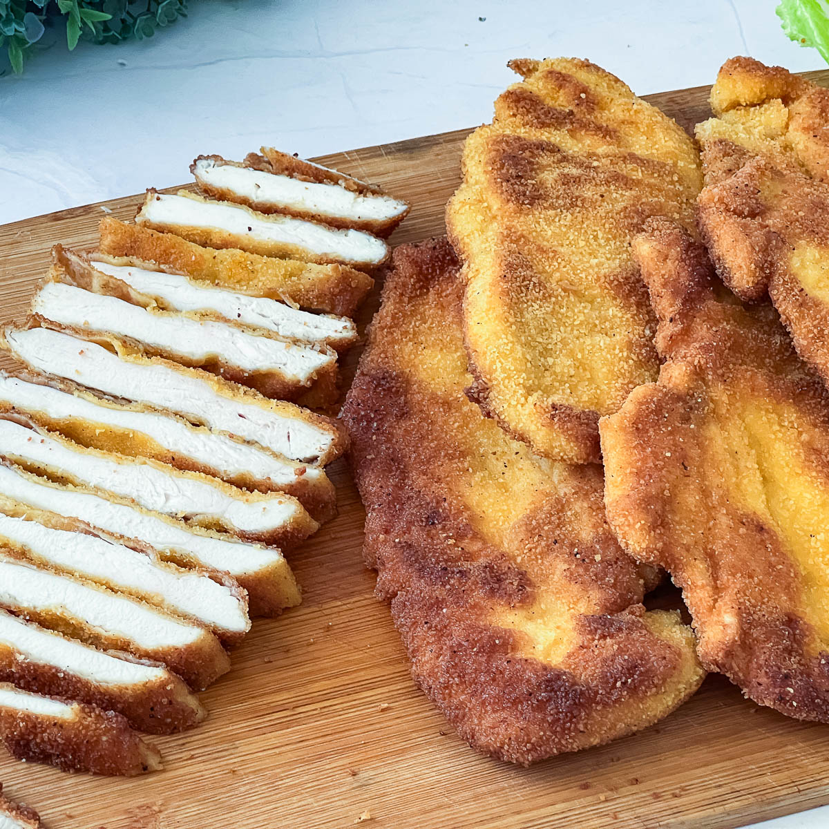 A sliced chicken schnitzel on a wooden board.