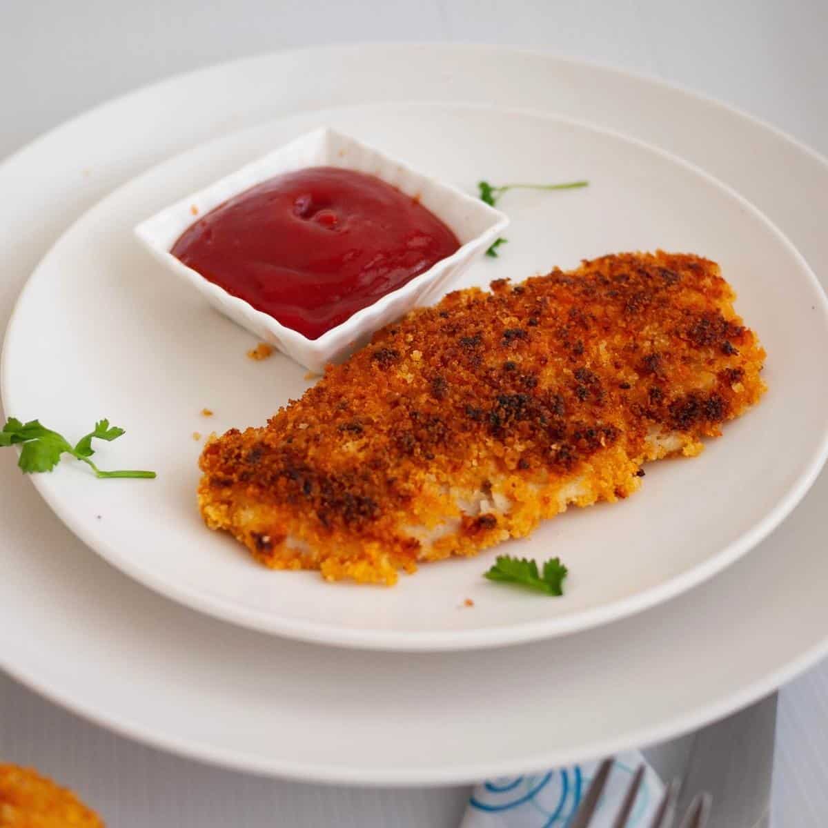 A schnitzel and ketchup on a plate.