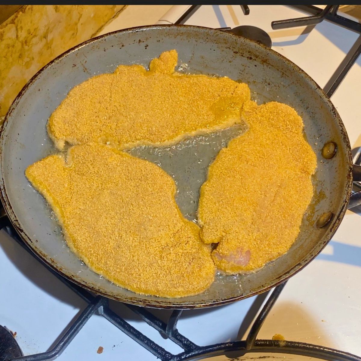 A frying pan with breaded chicken schnitzel.