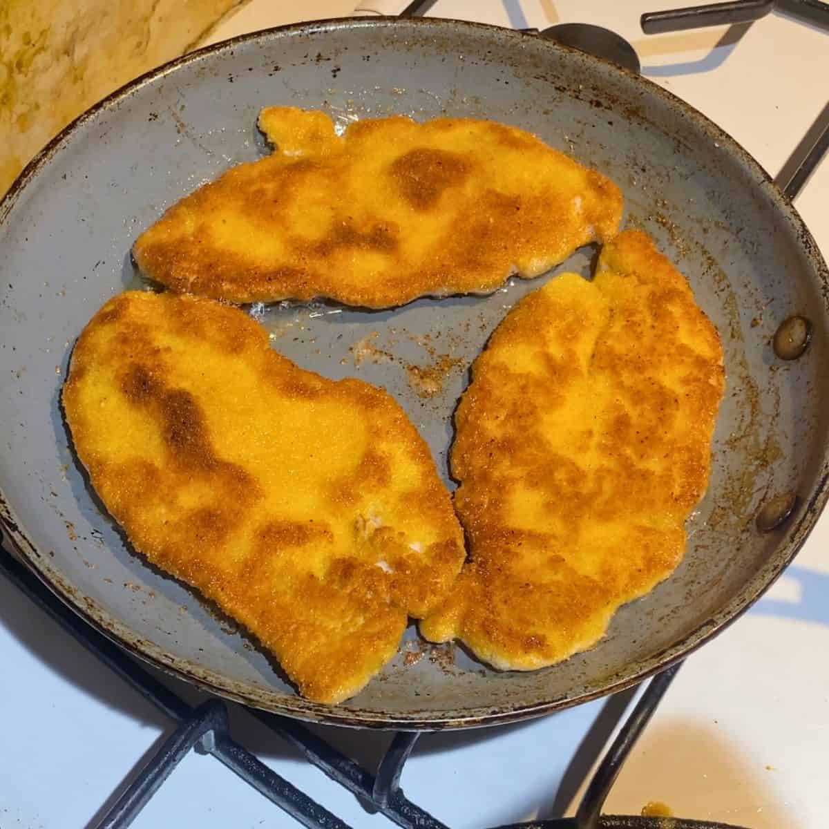 A frying pan with pan fried chicken breast.
