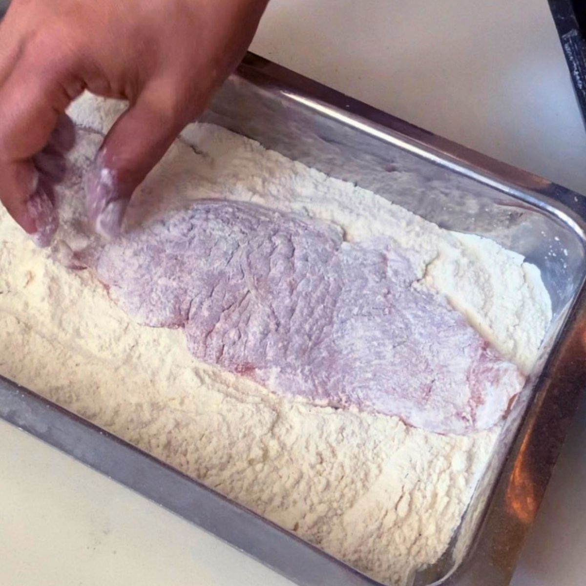 Coating chicken breast with flour.