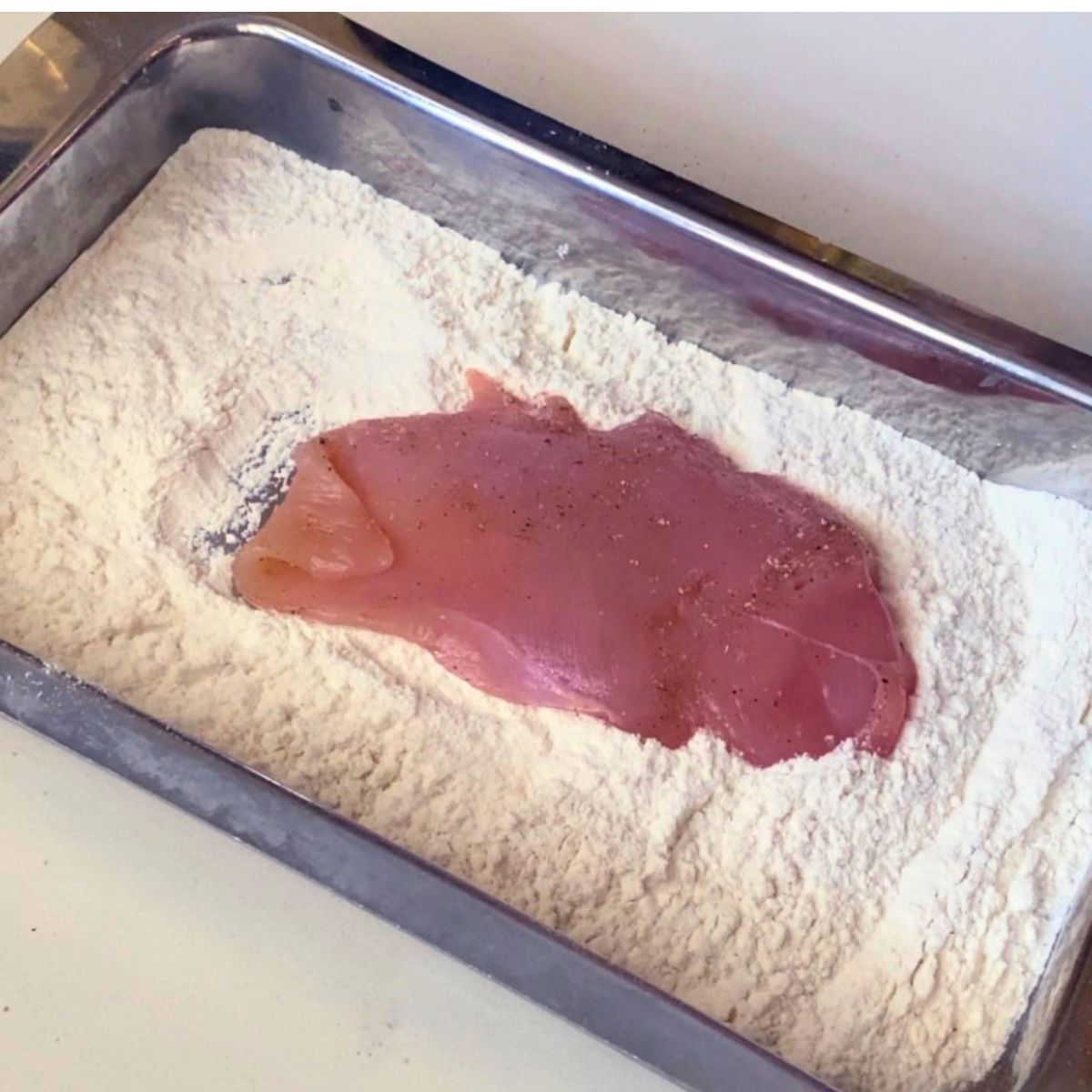 A tray with flour to coat the chicken breast.