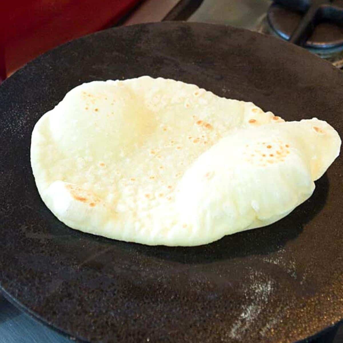 Naan cooking on a stovetop skillet.
