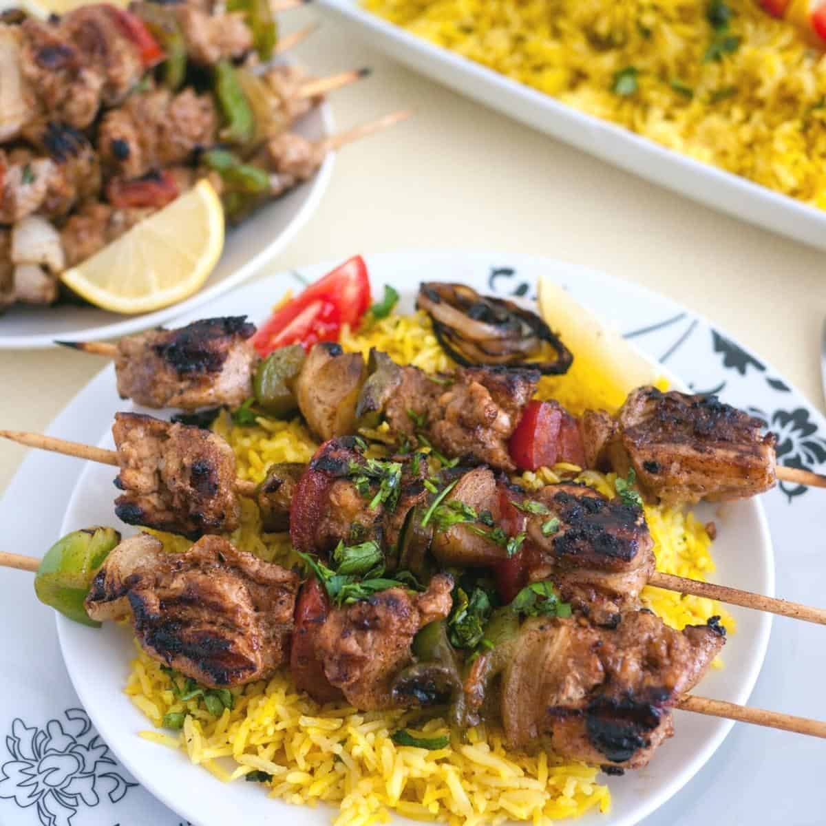 A plate with yellow rice and chicken on skewers.
