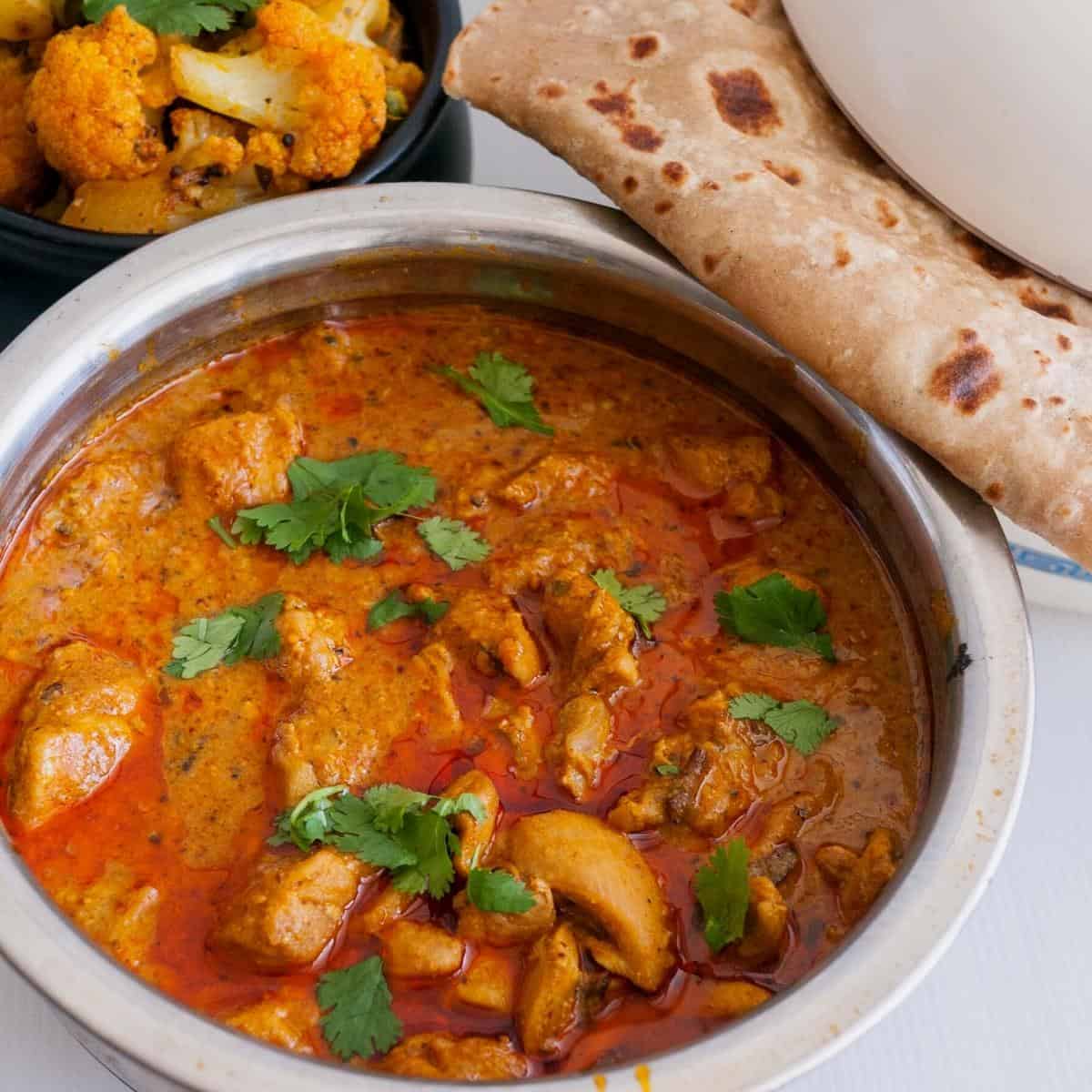Chicken curry in a pot with chapati on the side.