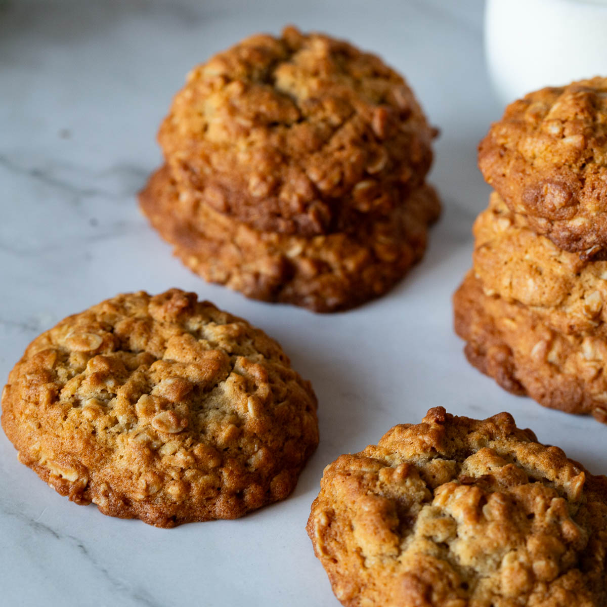 Soft and chewy oatmeal cookies stacked on white plate with glass of milk
