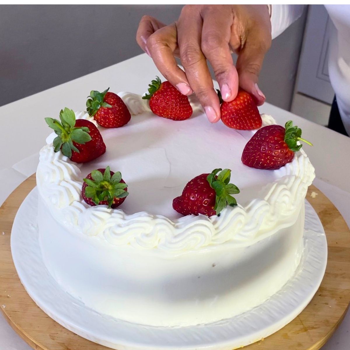 Step by step adding fresh strawberries on top of a cake.