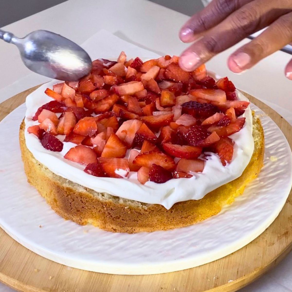 Adding fresh strawberries and cream to a light sponge cake.