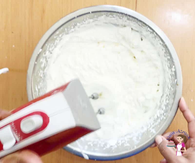 A person whipping cream in a bowl with a hand mixer.
