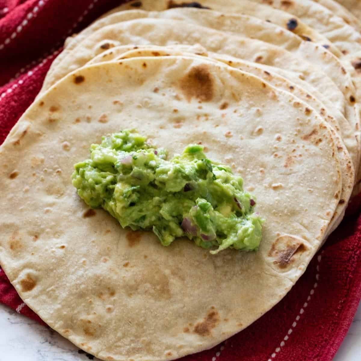 Stack of tortillas with guacamole on top.