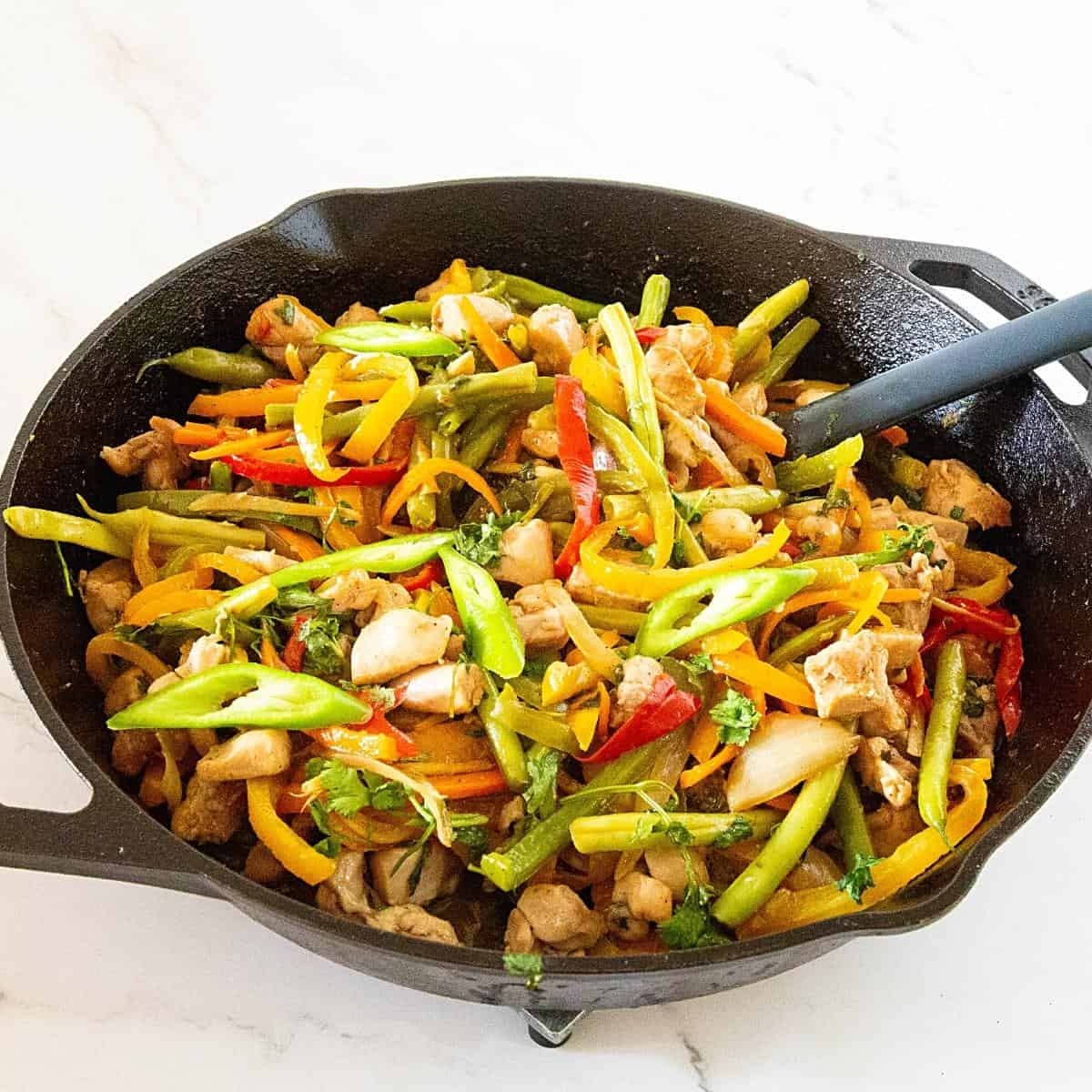 A large skillet with stir fried chicken and vegetables.