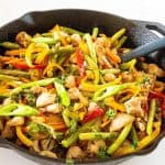 A skillet with chicken stir fry and veggies.