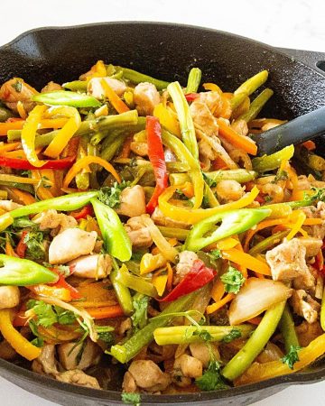 A skillet with chicken stir fry and veggies.