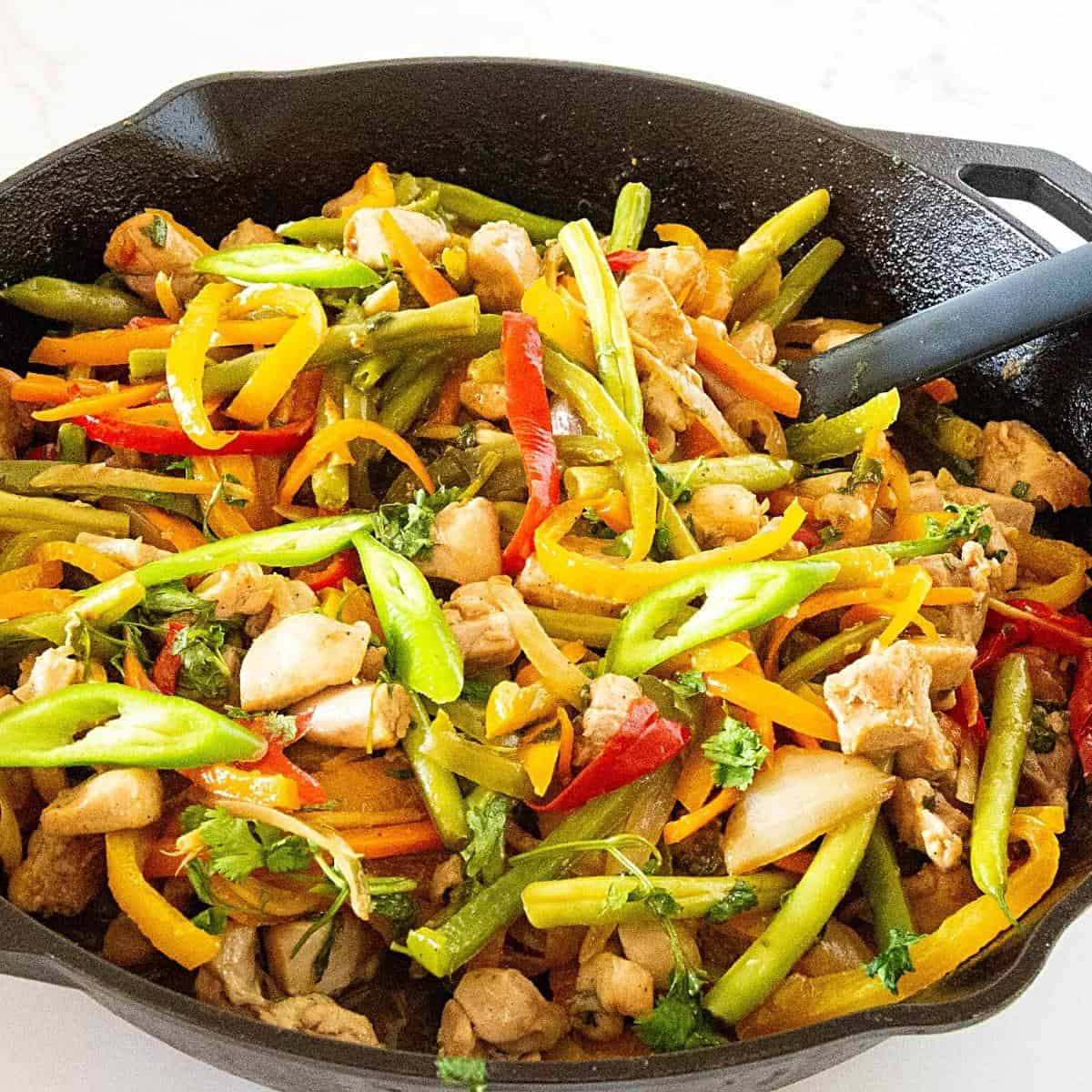 A skillet with chicken stir fry and veggies. 