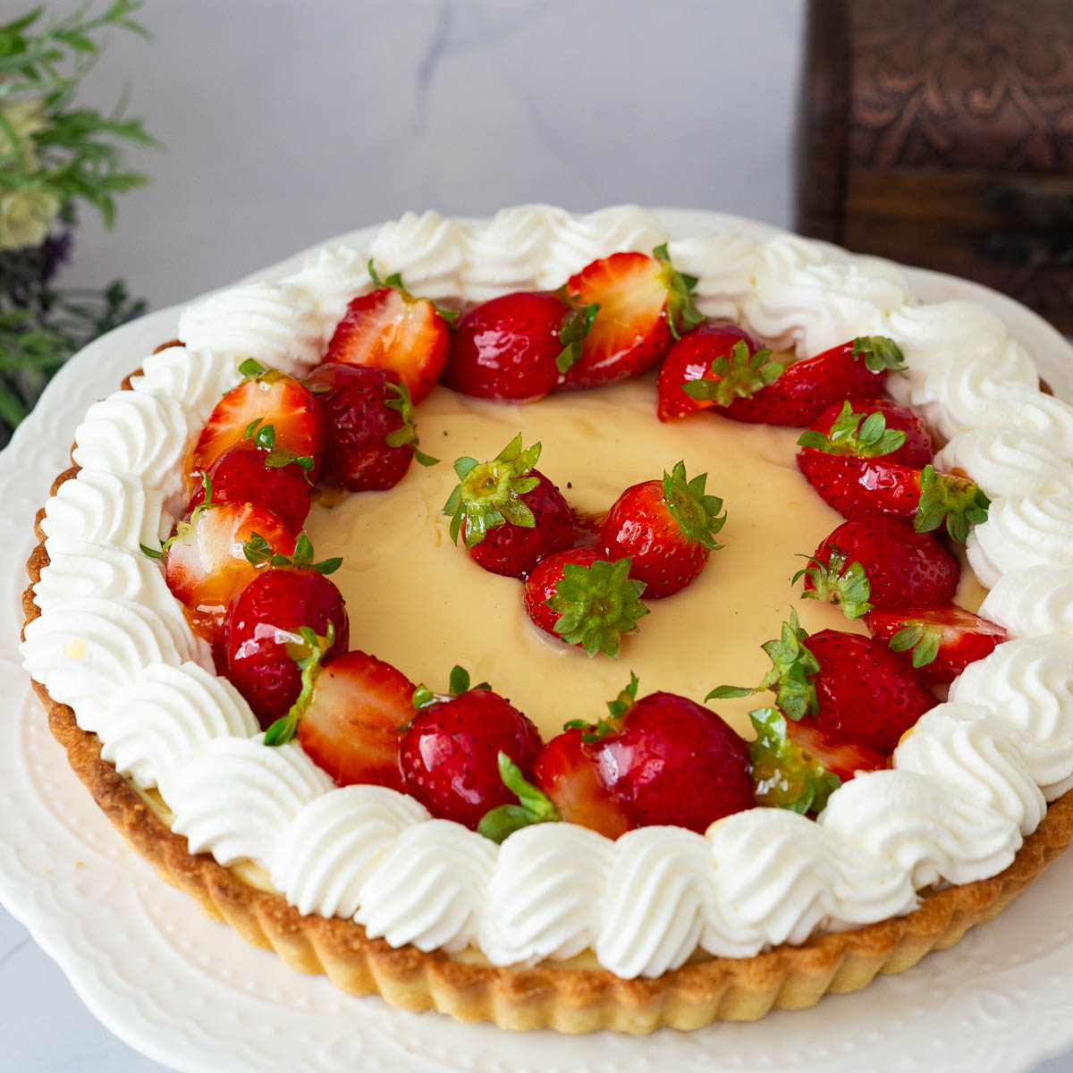 A frosted pastry cream tart with strawberries on a cake stand.
