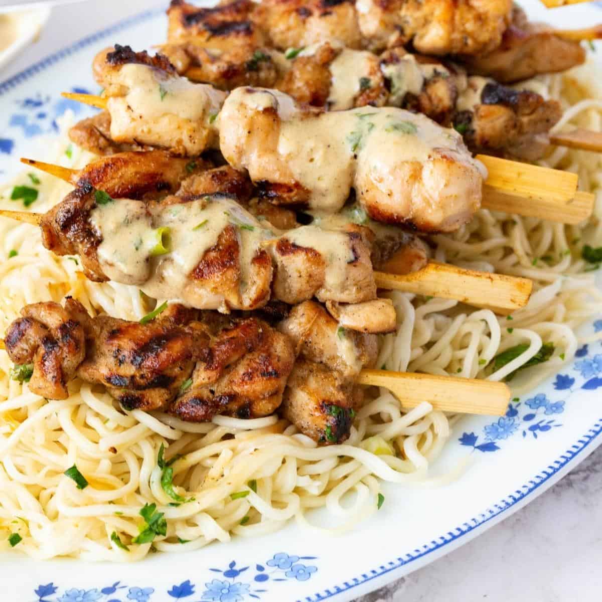 A plate with chicken on skewers over sauce.