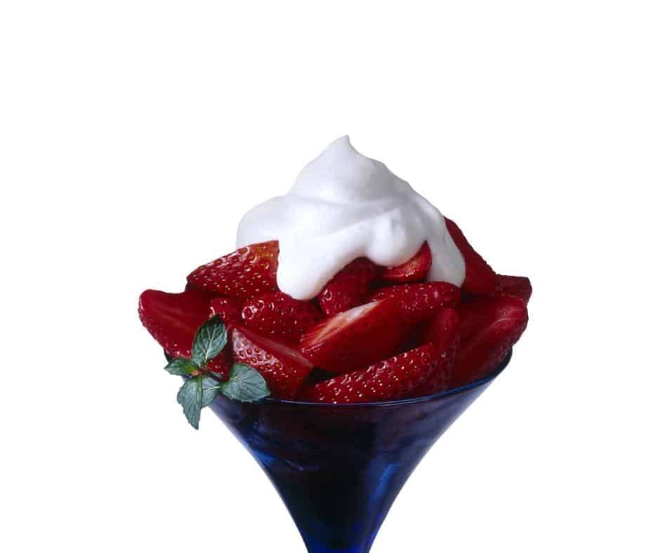 A glass full with strawberries and topped with cream.