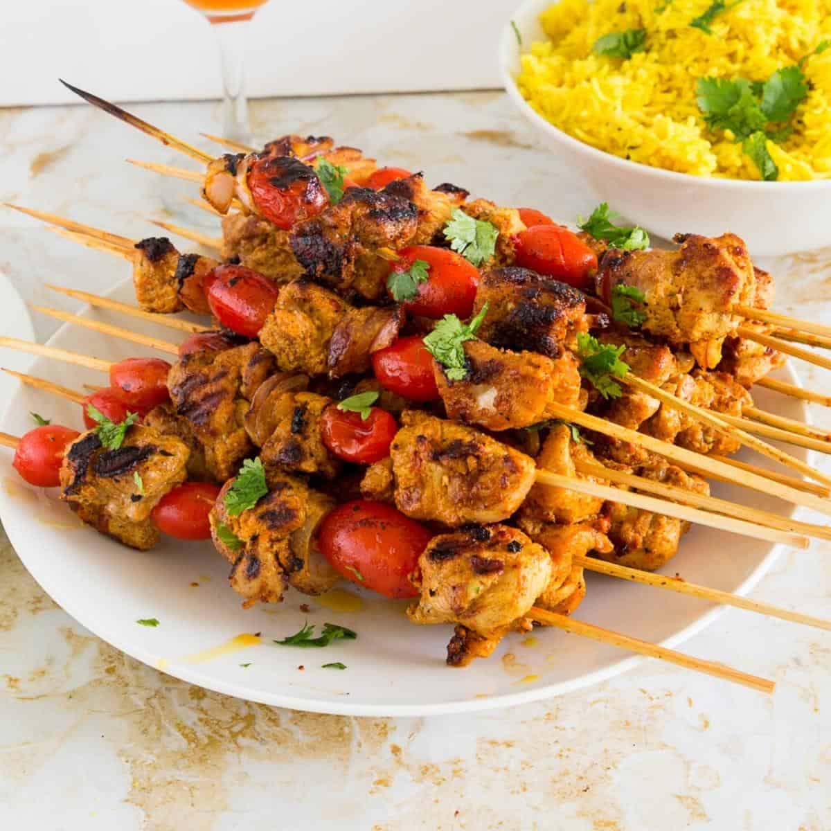 Chicken kebabs on a plate besides turmeric rice.