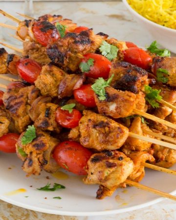 Skewered chicken kebabs on a plate with turmeric rice.
