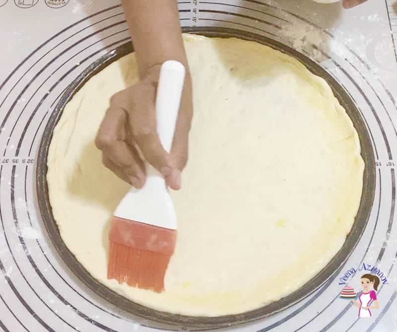 A person brushing the edges of a pizza dough with olive oil.