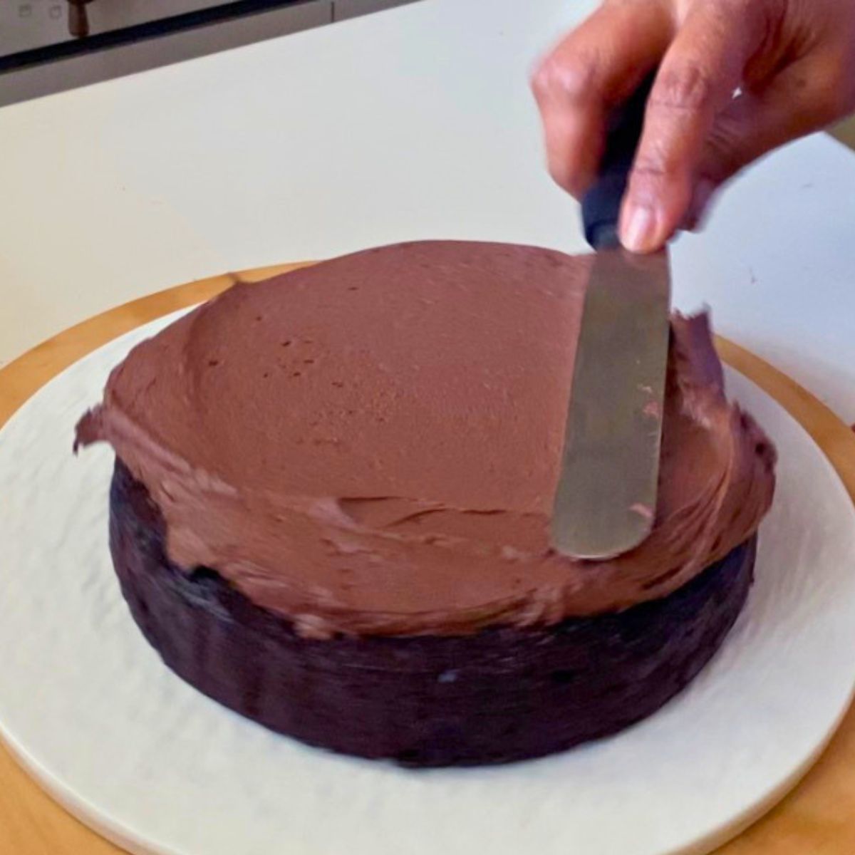 Adding chocolate frosting to the chocolate cake.