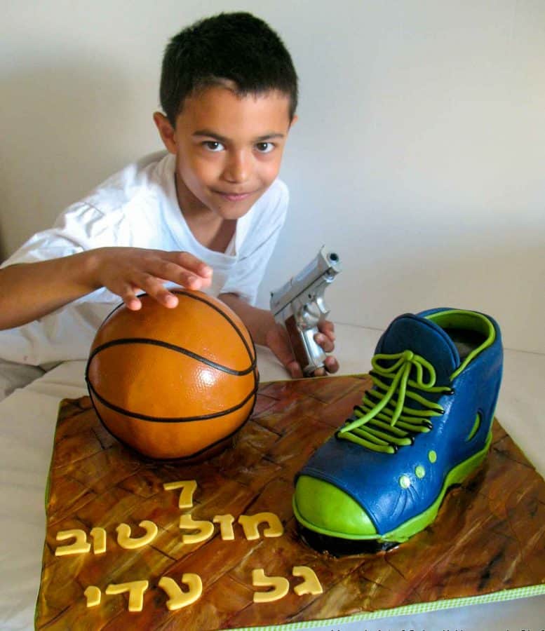 A boy next to a cake decorated like a basketball and a shoe.