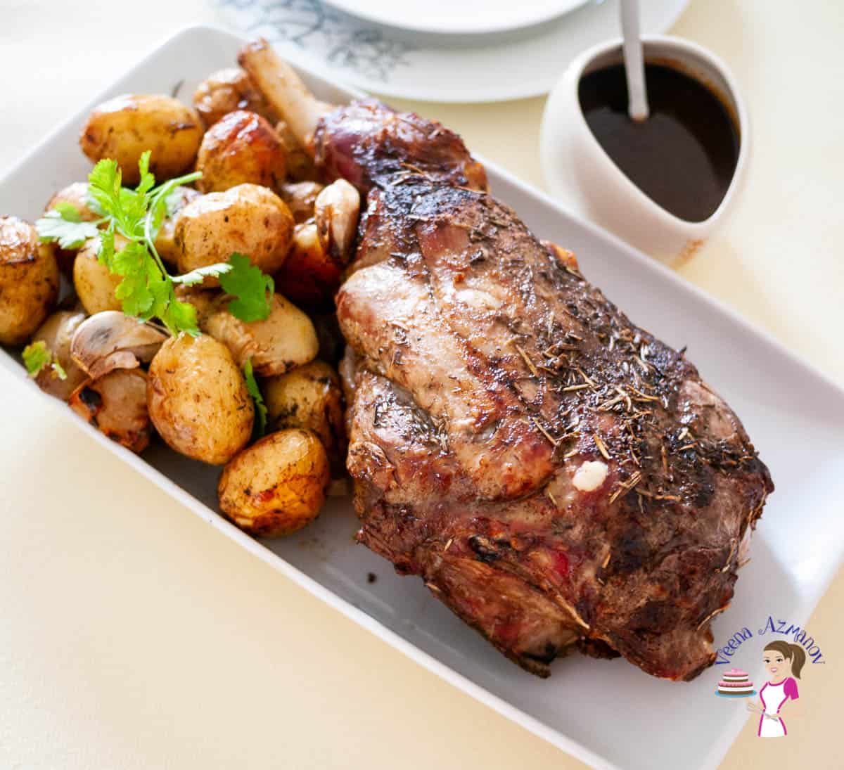 A roast leg of lamb with baked potatoes on a serving dish.