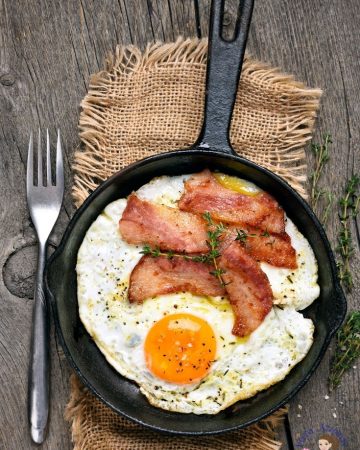A skillet with sunny side up egg and bacon.