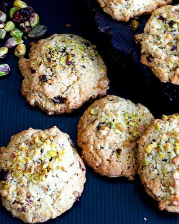 Cookies on a table with some pistachios and cranberries.