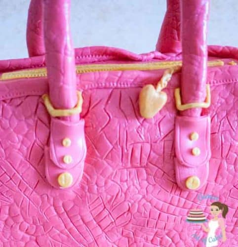 A close up of a cake sculpted to look like a pink handbag.