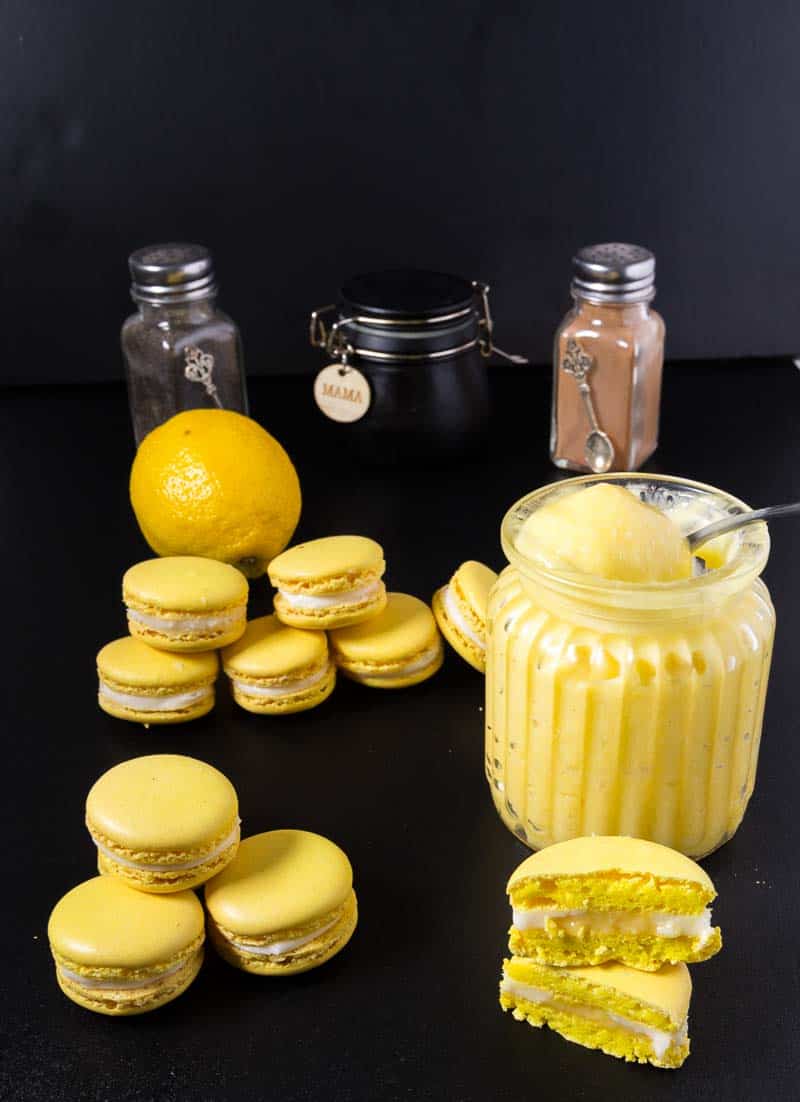French Macarons are on-trend all year round. These lemon French macarons filled with lemon curd and Swiss meringue buttercream are especially refreshing and light. This simple, easy and effortless recipe uses my full proof macaron recipe as a base so you can make these successfully over and over again. People are going to think you are a macaron master baker!! A Pinterest Optimized image for Lemon French Macarons fill with homemade lemon curd and Swiss meringue buttercream using my full proof french macaron recipe