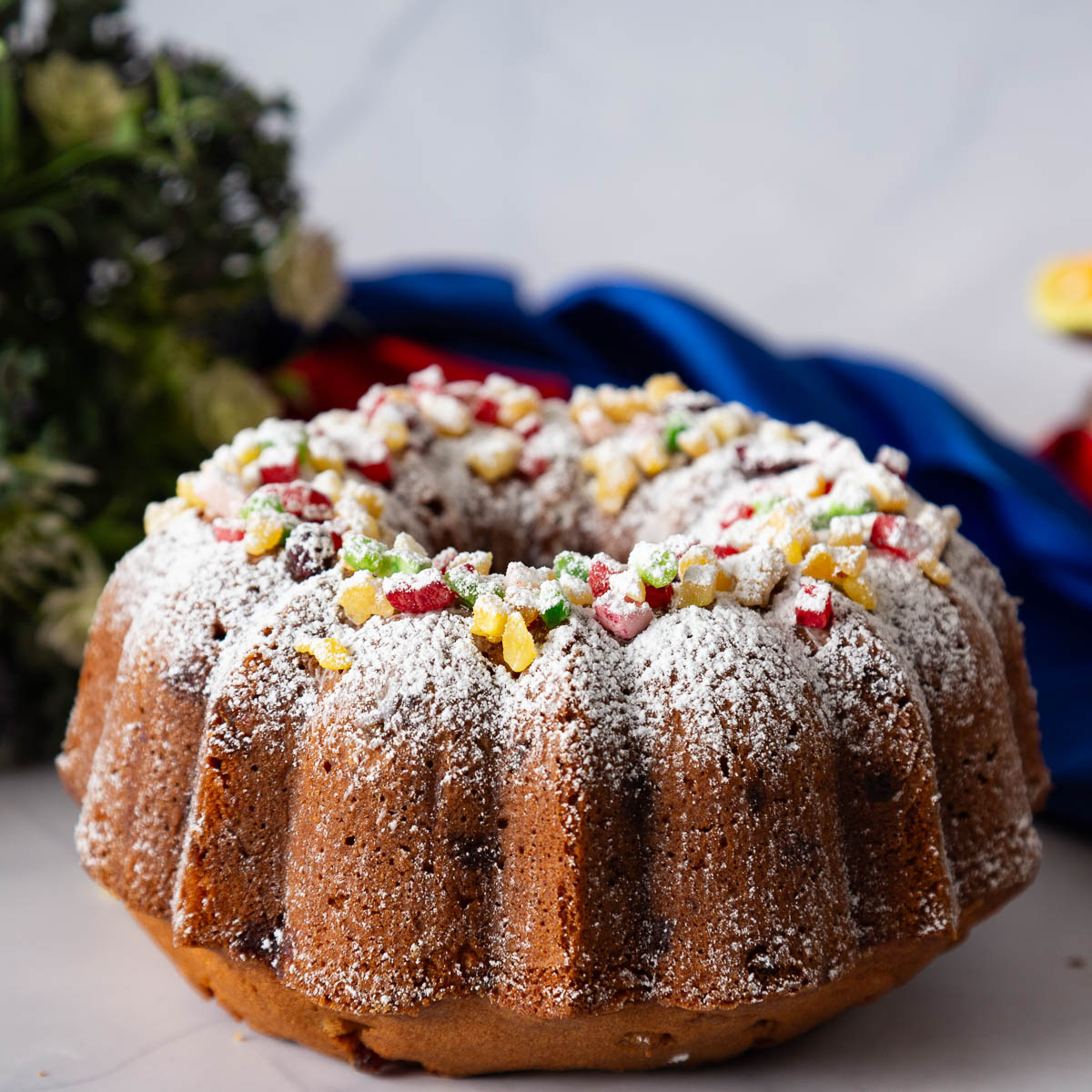 Bundt fruitcake topped with powdered sugar and colorful candied fruit.