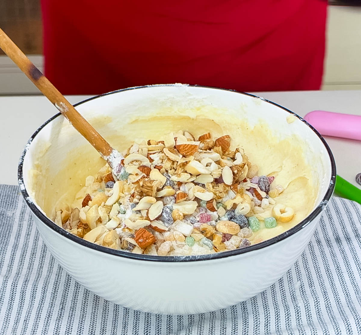 Fruitcake batter with candied fruit and nuts in a while bowl.