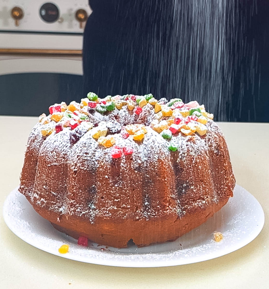 Overhead view of a glace fruit cake in a bundt shape dusted with powdered sugar.