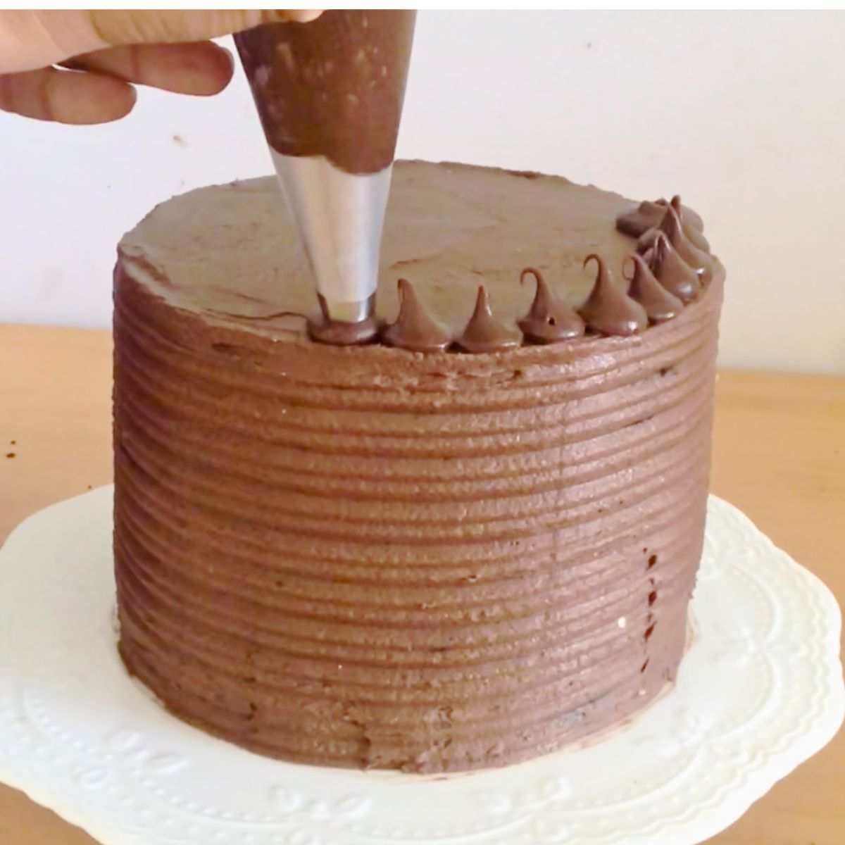 Piping small chocolate kisses on a chocolate cake.