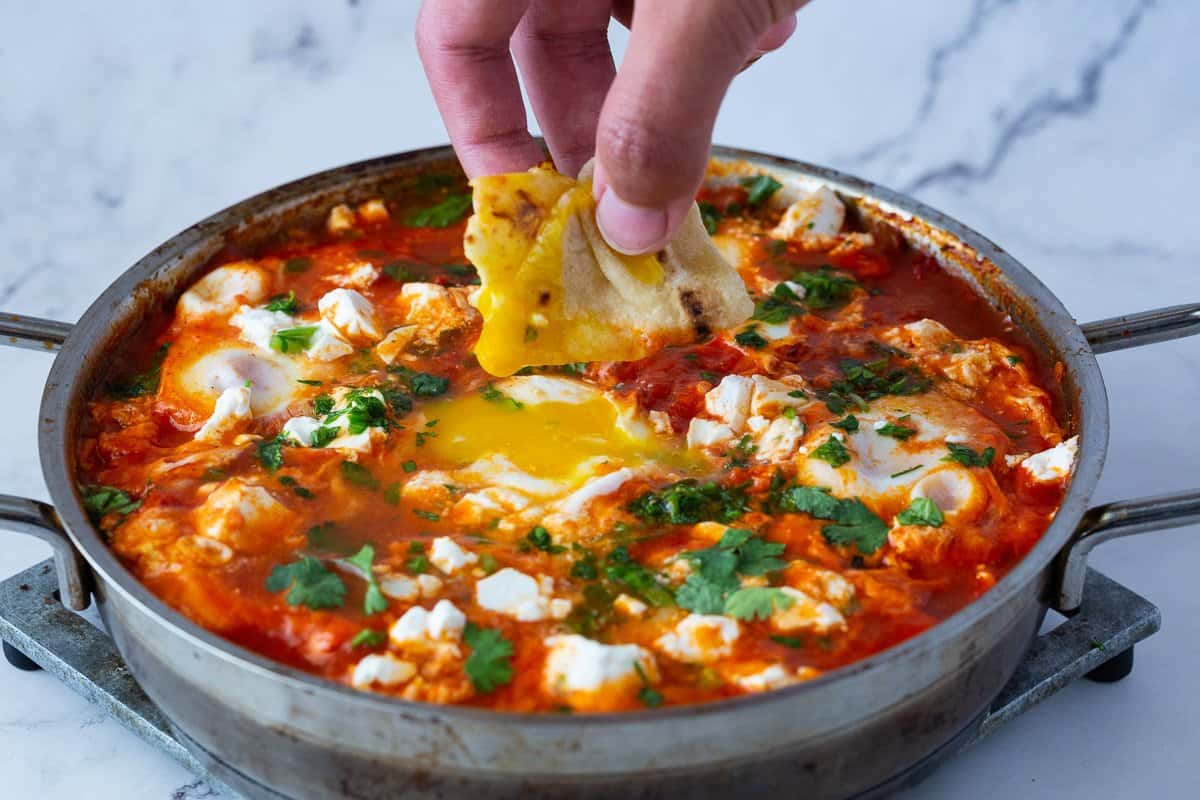 A large skillet with egg shakshuka and crumbled cheese.