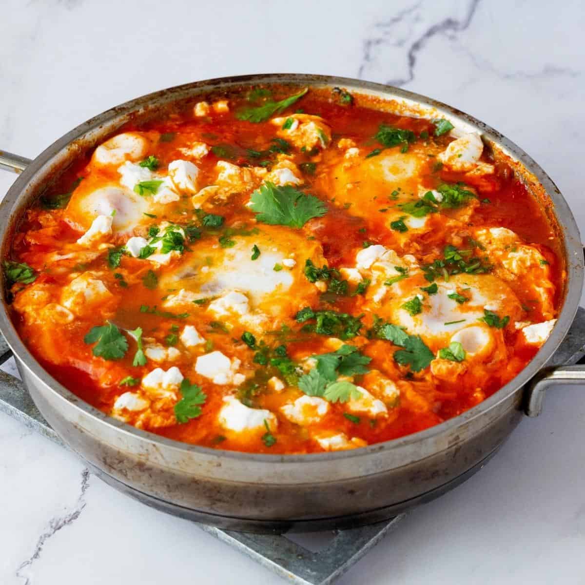 A large skillet with egg shakshooka and crumbled cheese.