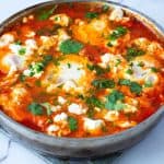 A large skillet with egg shakshooka and crumbled cheese.