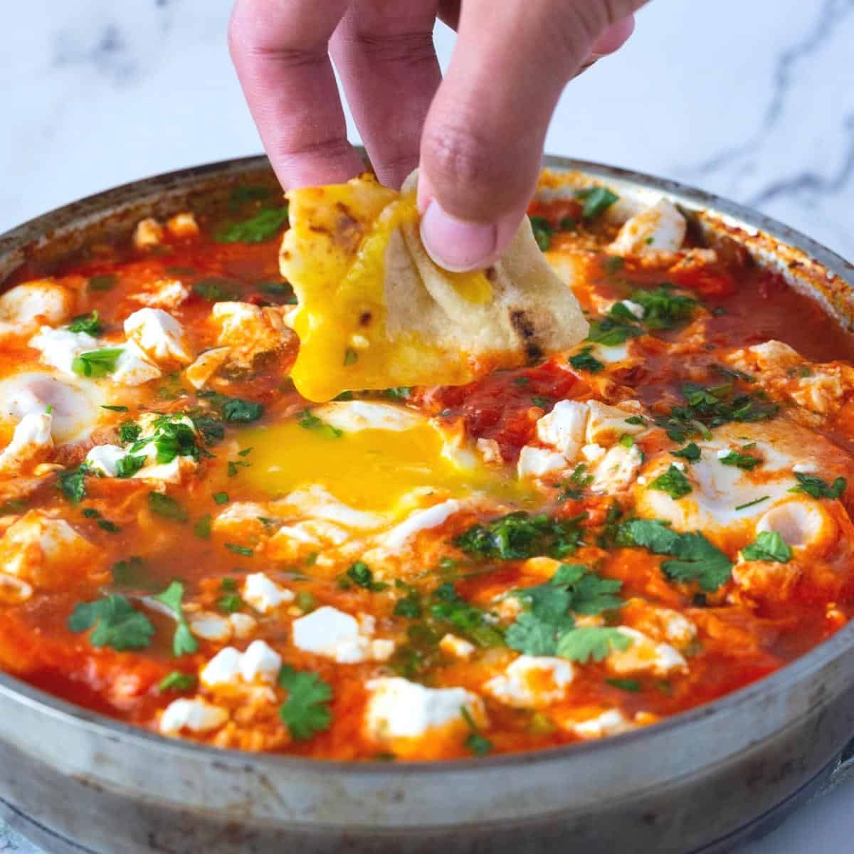 A large skillet with egg shakshooka and crumbled cheese.