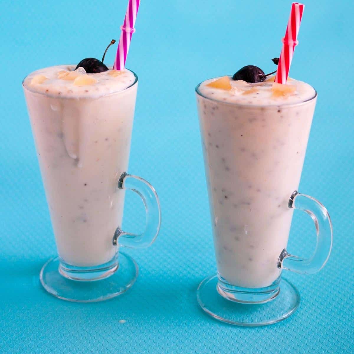 Two tall glasses of smoothie topped with crushed pineapple