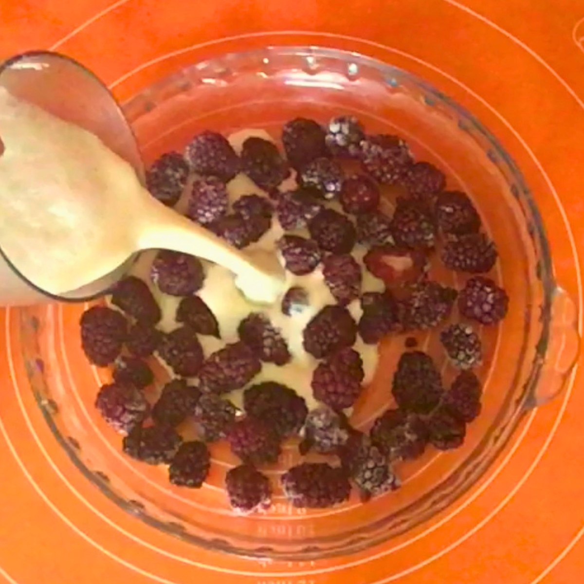 Pouring custard over the blackberries in pie pan.