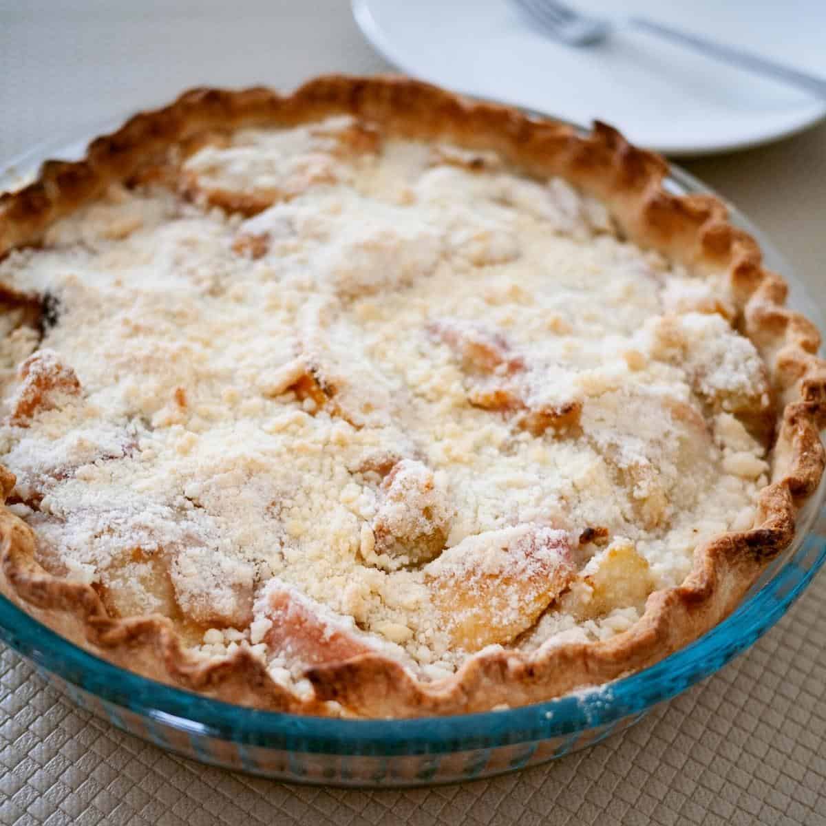 A pie pan with peach pie topped with crumble.