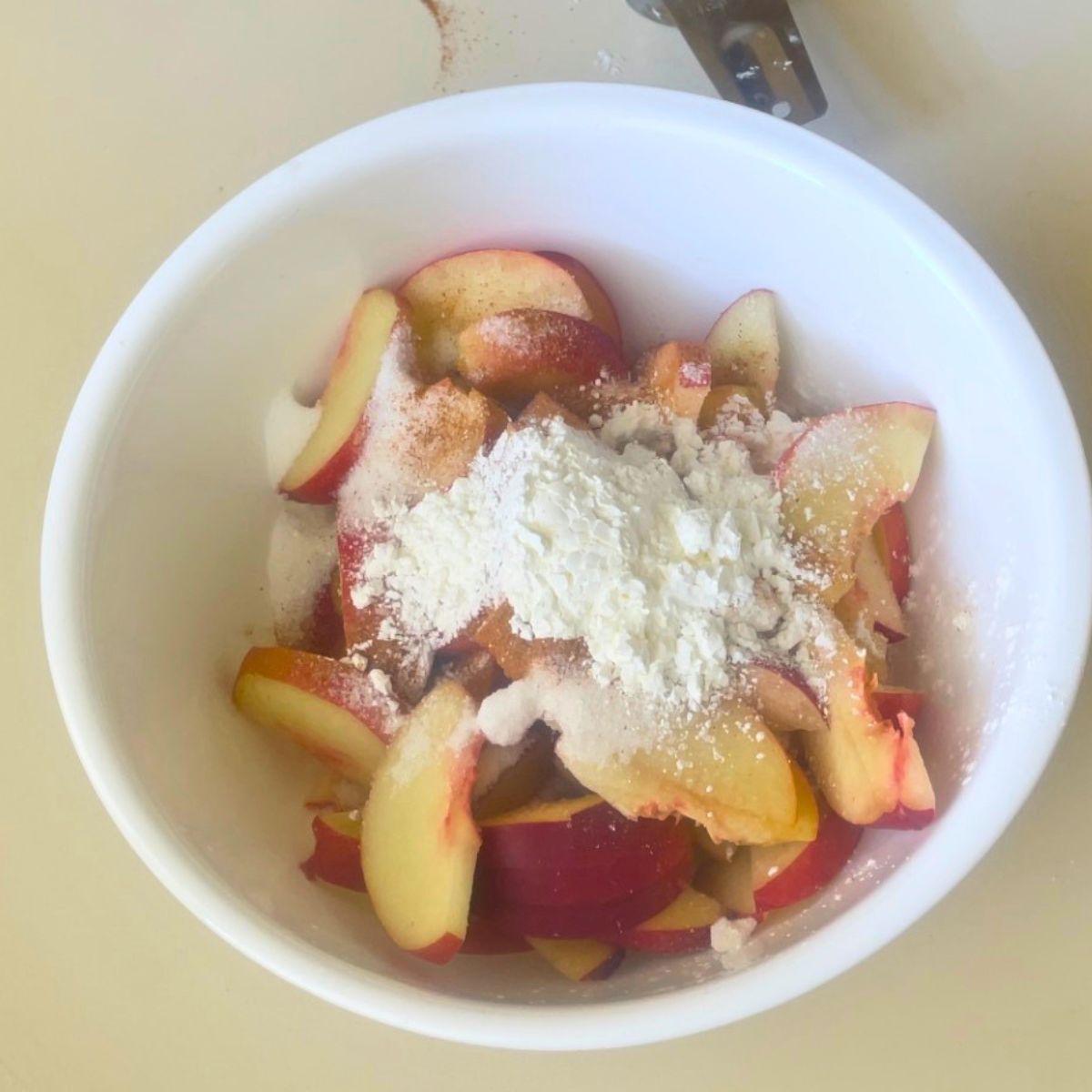 Making peach pie filling in a white bowl.